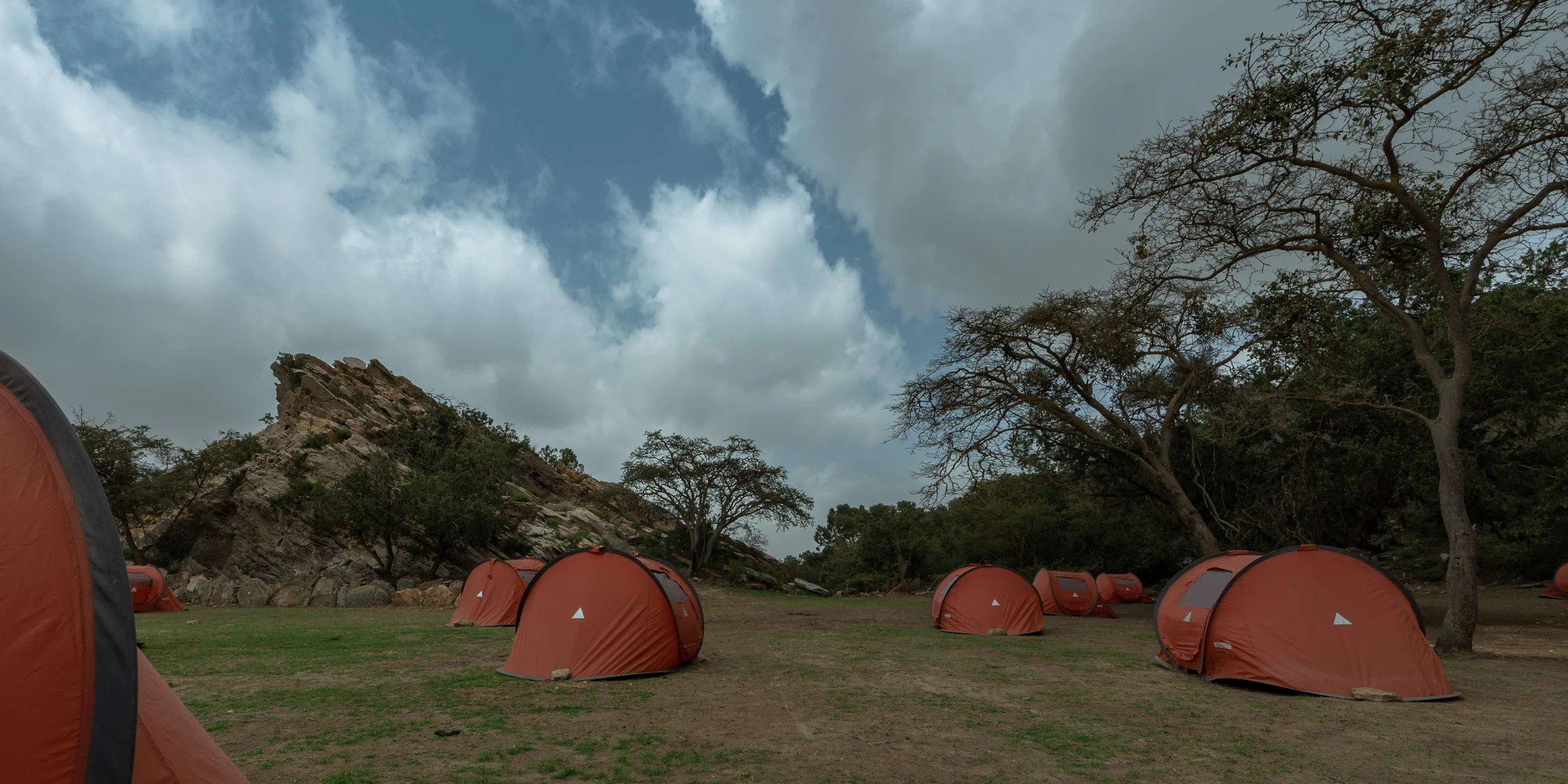 Orange tents pitched on a meadow below a rocky outcrop